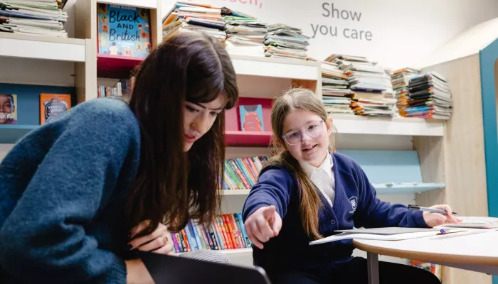 A pupil in a dark blue jumper points at a laptop as she learns with her tutor. 
