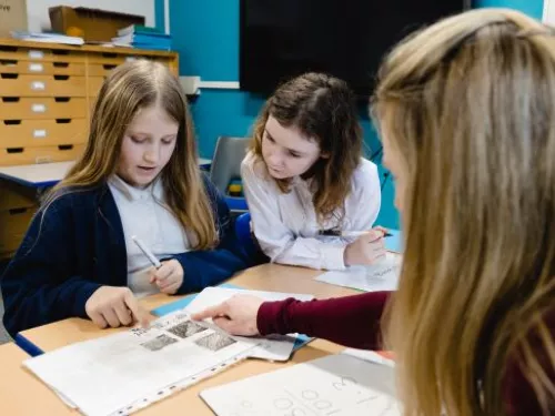 Two pupils study a written piece of work with their tutor