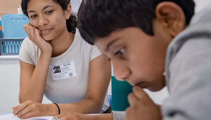 A tutor looks on as a pupil concentrates on a piece of written text.