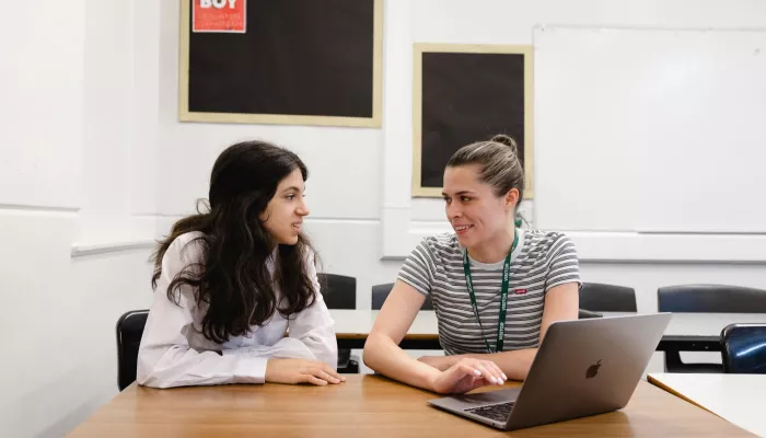 A tutor and pupil are discussing content on a laptop. Both are smiling.