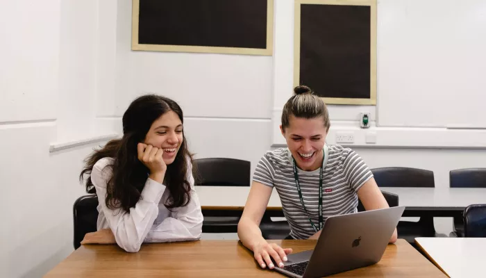 A female tutor, and female pupil are smiling as they study together.