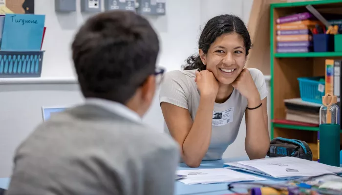 A tutor smiles at a pupil as they work together on a topic for reading.