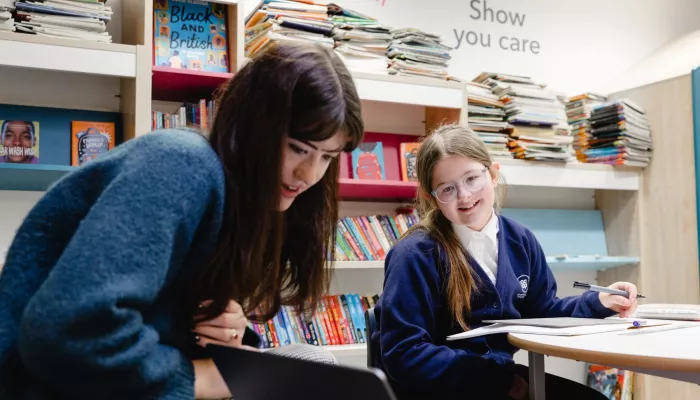 A tutor and pupil look at content on a laptop. Both are smiling.