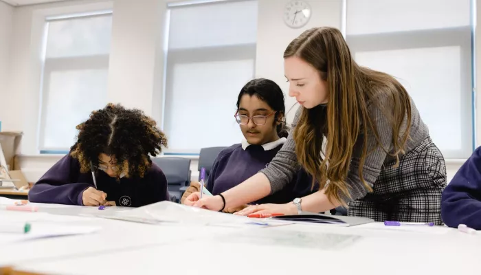 A tutor writes as a pupils looks on. A second pupil is focused on their writing.