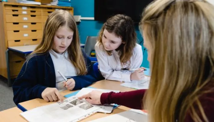 Two pupils study a written piece of work with their tutor