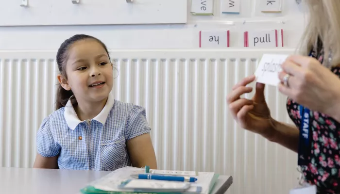 A young child smiles as she learns a word in a phonics session