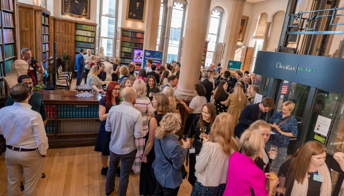 A group of people wearing formal wear are gathered at Tutor Trust's annual Summer Reception. They are in a formal room and are talking in small groups.