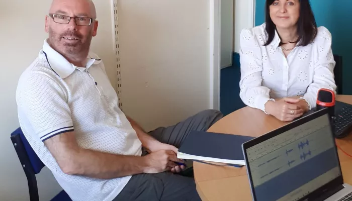 Two people are sitting at a round table.  There is a laptop open in front of them.