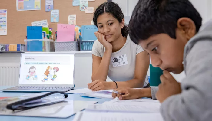 A pupil works on some writing while the tutor looks on