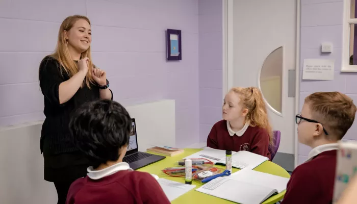 A tutor is smiling as she works with a group of Year 6 pupils on reading