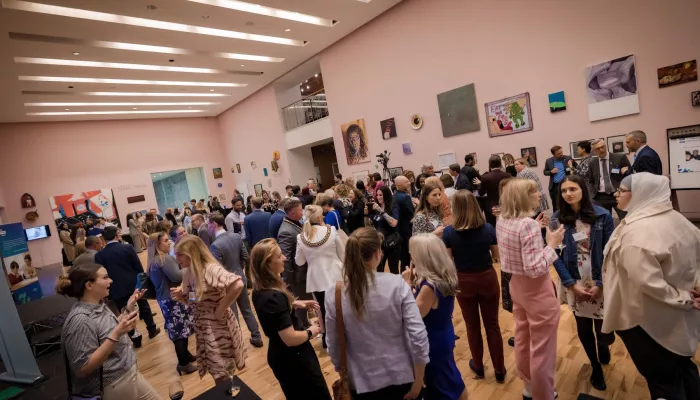 A crowd of people are chatting and mingling in the gallery space