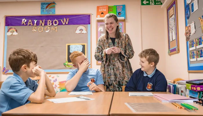 a female tutor smiles as she gives a class to three boys