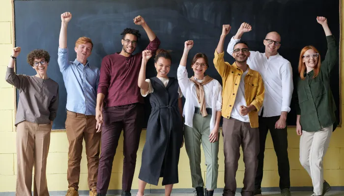 four men and two women raise a celebratory hand in front of a chalkboard