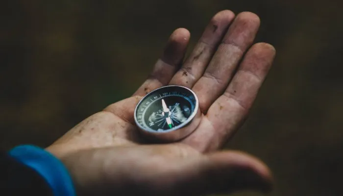 a child's muddy hand holding a small metal compass