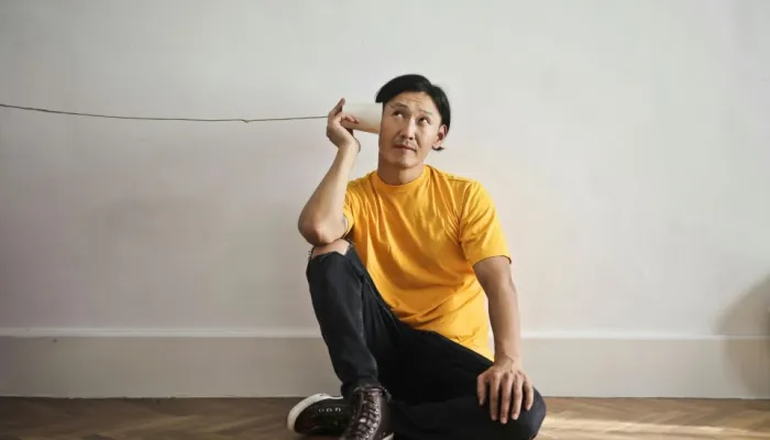 a man in a yellow t-shirt listens to a cup attached to some string