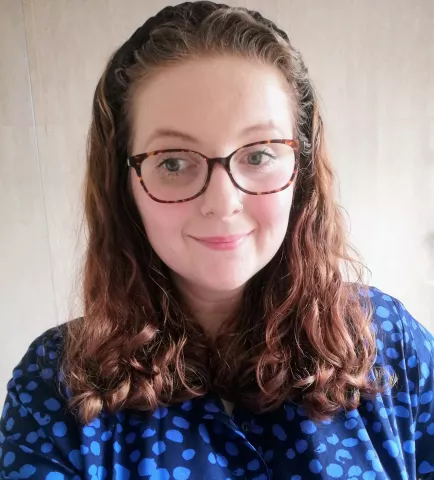 Fran is keen to dismantle barriers to learning for pupils. Fran has shoulder-length brown hair, is wearing a blue dress and has glasses.