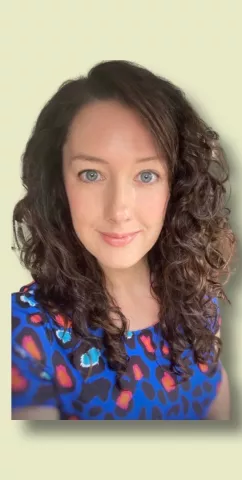 Helen has long dark hair with curls and a floral dress. She looks into the camera smiling.