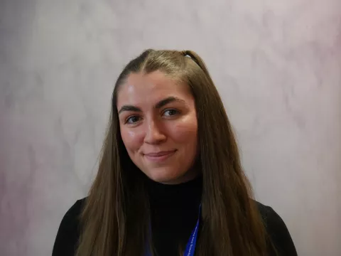 Eva has long, straight dark hair and smiles to the camera.