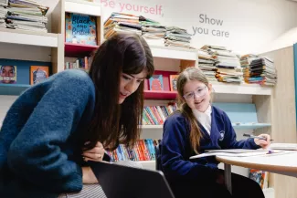 A tutor and pupil look at content on a laptop. Both are smiling.