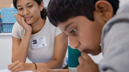 A tutor looks on as a pupil concentrates on a piece of written text.