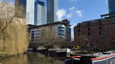 Canal around Castlefield Bowl, Manchester, with small boats parked in the water and skyscrapers in the background.