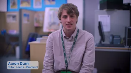 Male tutor in a smart white shirt and short hair, sitting and enthusiastically talking about his tutoring experience.