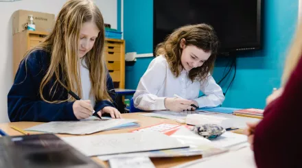 Two pupils are smiling as they write in exercise books