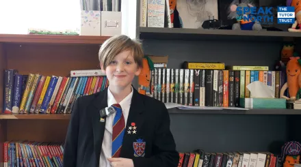 Pupil James wears a black blazer with several achievement badges on the sides, white shirt, and blue and red striped tie. He excitedly tells us how it feels to be a competition winner.