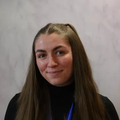 Eva has long, straight dark hair and smiles to the camera.