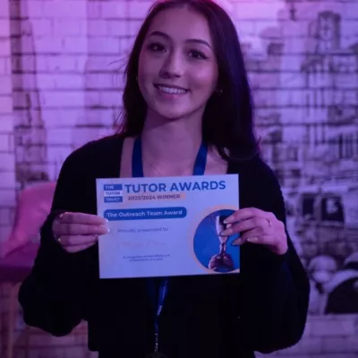 A young woman with long dark hair holds a winner's certificate