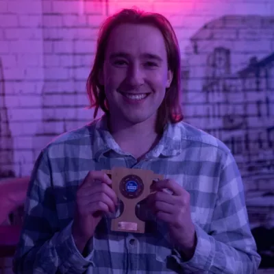 A young male in a checked shirt with long hair holds a wooden trophy