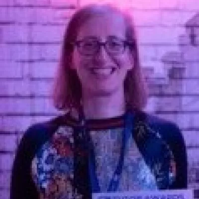 A woman with red hair and glasses smiles and holds a winner's certificate