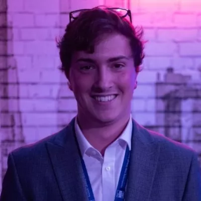 A young man in a suit jacket and white shirt smiles