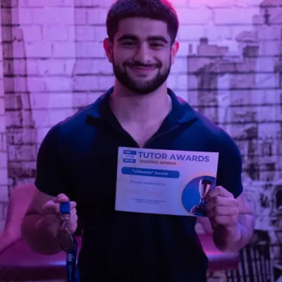 A young man in a dark t-shirt smiles and holds a winner's certificate