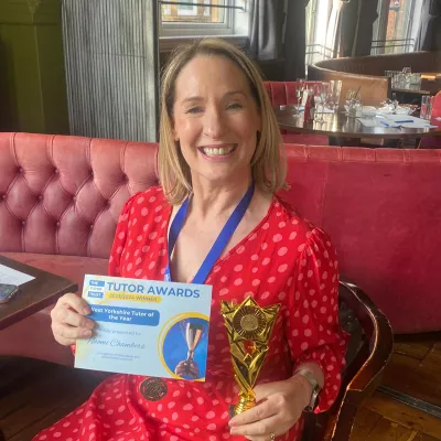 A woman with blonde hair wearing a red dress holds a certificate and trophy