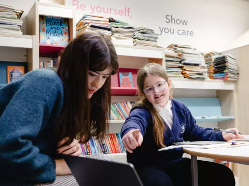 A young pupil points at a laptop in a lesson with her tutor.