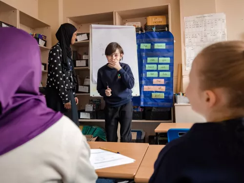 A tutor and pupils are having fun in a session, with the young boy at the front of the group stifling a giggle!