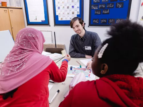 A male tutor, wearing a grey shirt, smiles as two pupils participate in a session.