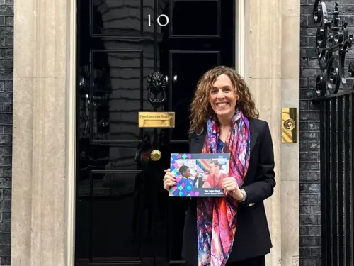 Abigail stands outside the distinctive door of Number 10 Downing Street, holding a copy of the Tutor Trust's 2022 Impact Report