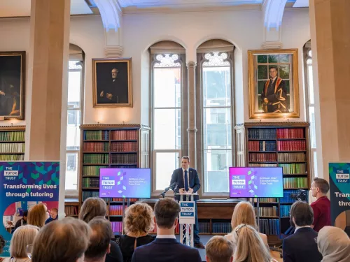 CEO Ed Marsh is addressing guests at the Summer Reception. He is standing at a lectern, in front of a large window, flanked by two bookcases.