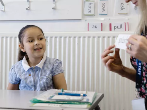 A young child smiles as she learns a word in a phonics session