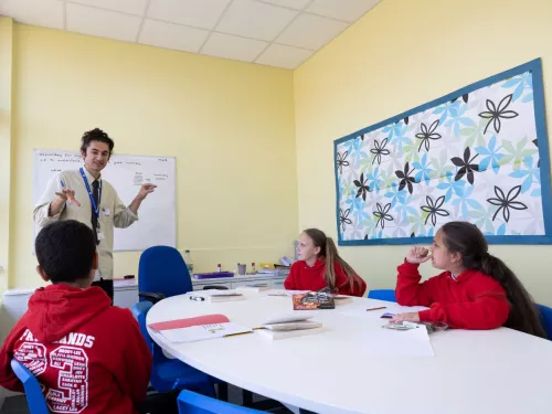 A tutor stands in front of a group of three pupils. The pupils are wearing red jumpers.