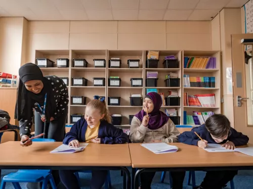 Three young pupils are working hard in a session, with one showing their work to the tutor.