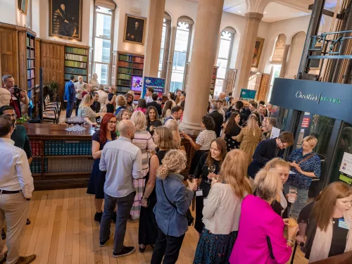 A group of people wearing formal wear are gathered at Tutor Trust's annual Summer Reception. They are in a formal room and are talking in small groups.