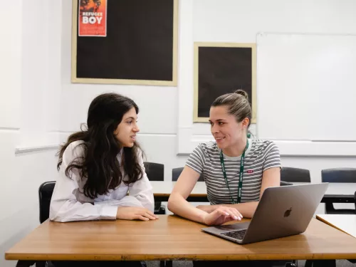 A tutor and a pupil work together, and are both looking at some content on a laptop