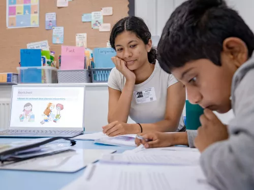 A pupil works on some writing while the tutor looks on