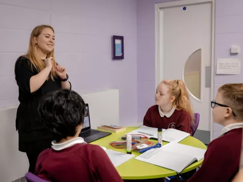 A tutor is smiling as she works with a group of Year 6 pupils on reading