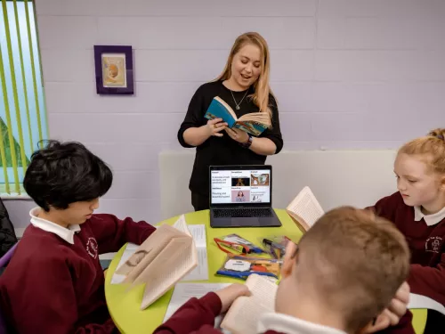 A tutor reads some text from a book to tutees