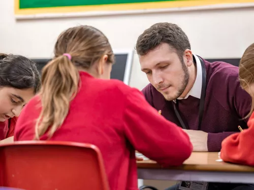 A tutor and pupil are looking closely at a piece of work.