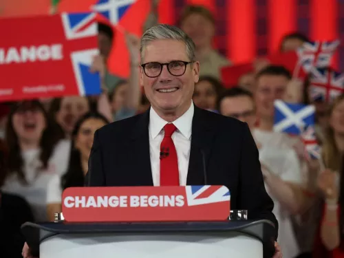 Sir Keir Starmer stands behind a podium wearing a red tie and smiling